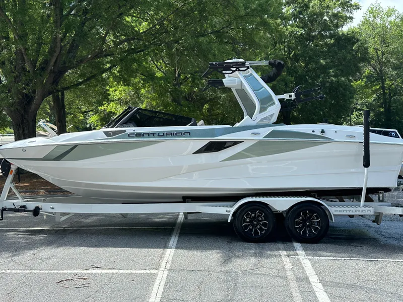 Slide: The Image of 2025 Centurion Fe23 boat on trailer, parked outdoors, surrounded by trees. - 14
