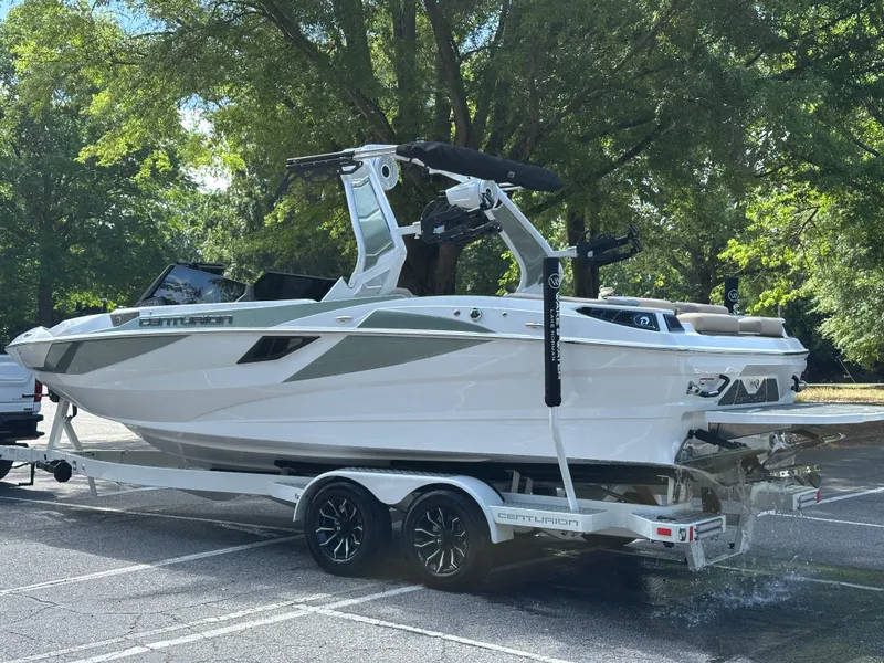 Slide: The Image of 2025 Centurion Fe23 boat on trailer in parking lot, surrounded by trees. - 15