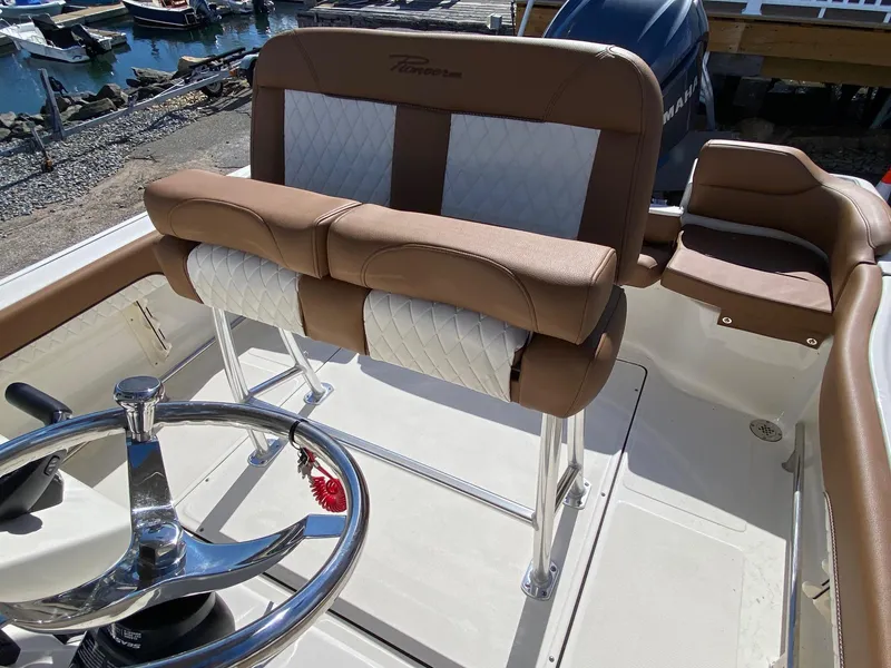Slide: The Image of 2025 Pioneer 222 Islander boat interior with brown and white seating, steering wheel, and dock view. - 6