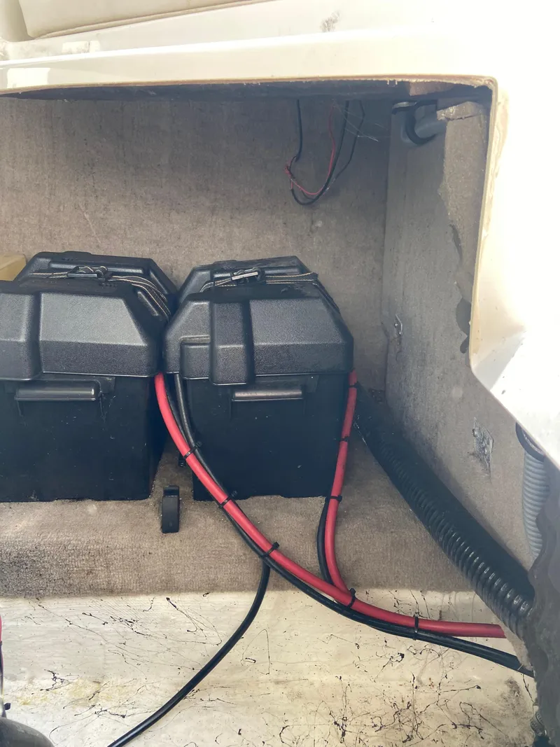 Slide: The Image of 2008 Ebbtide 2700 SS Bow Rider battery compartment with two black battery boxes and red cables. - 23
