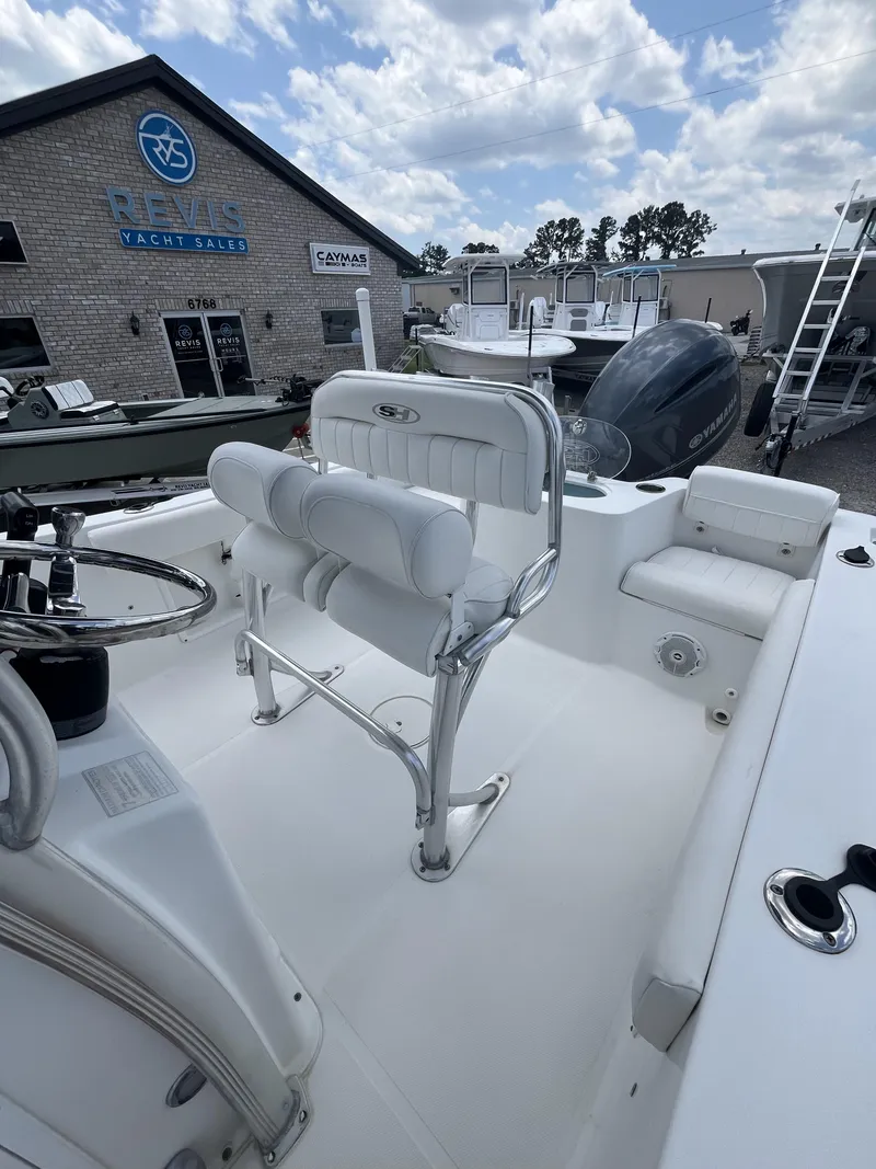 Slide: The Image of 2018 Sea Hunt Triton 210 boat interior with seating, steering wheel, and dealership in background. - 15