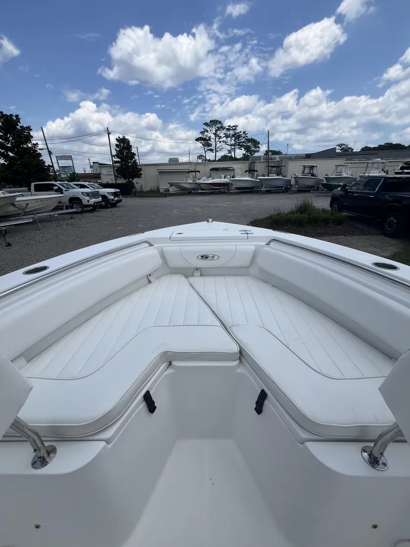 Slide: The Image of 2018 Sea Hunt Triton 210 boat with white seating, parked outdoors under a partly cloudy sky. - 6