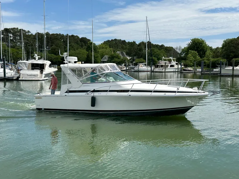 Slide: The Image of 1994 Bertram 30 Express Fisherman boat cruising in a marina with trees and yachts. - 2