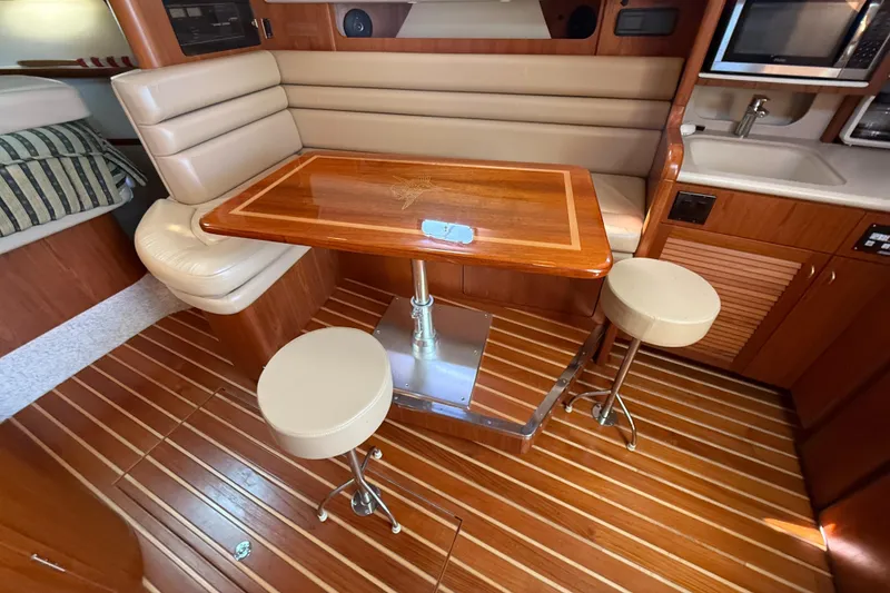 Slide: The Image of 2002 Pursuit 3800 Express yacht interior with wooden table, stools, and kitchenette. - 42