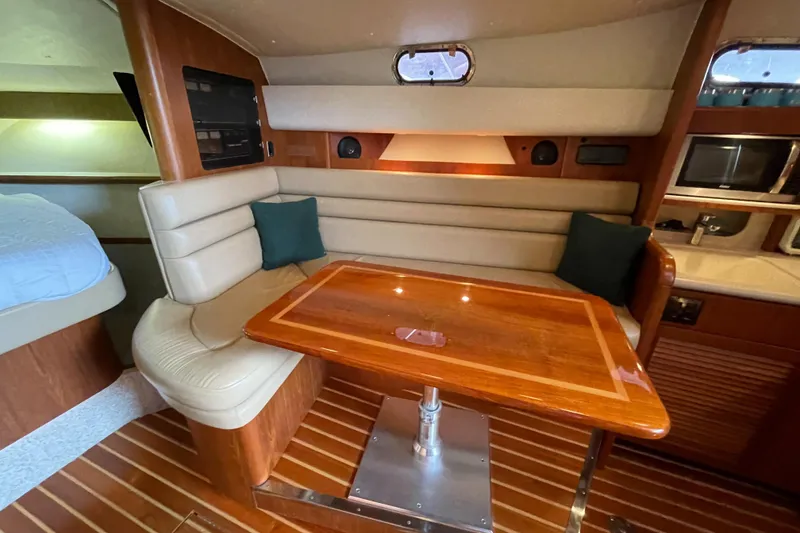 Slide: The Image of 2002 Pursuit 3800 Express yacht interior with wooden table, cushioned seating, and modern amenities. - 48