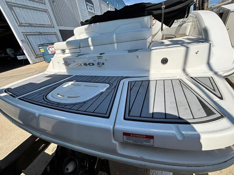 Slide: The Image of 2013 Sea Ray 240 Sundeck boat with spacious deck and seating, docked near a warehouse. - 6