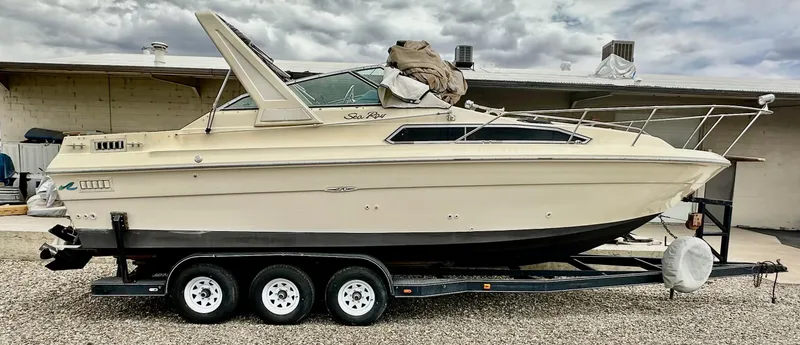 Slide: The Image of 1987 Sea Ray 270 Sundancer boat on a triple-axle trailer, parked outdoors. - 2