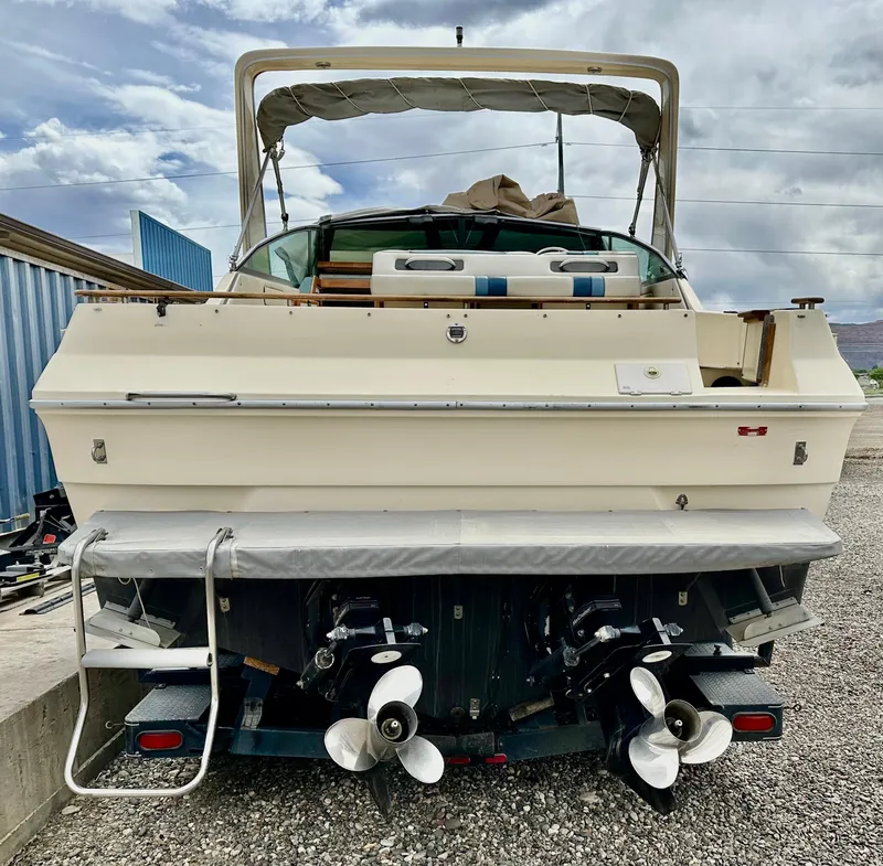 Slide: The Image of 1987 Sea Ray 270 Sundancer boat, rear view with dual propellers, parked on gravel. - 4