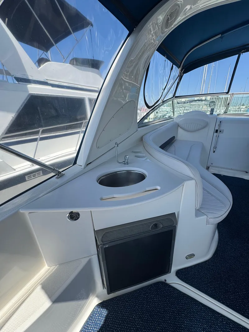 Slide: The Image of 2006 Bayliner 325 boat interior with sink and seating under blue canopy. - 10