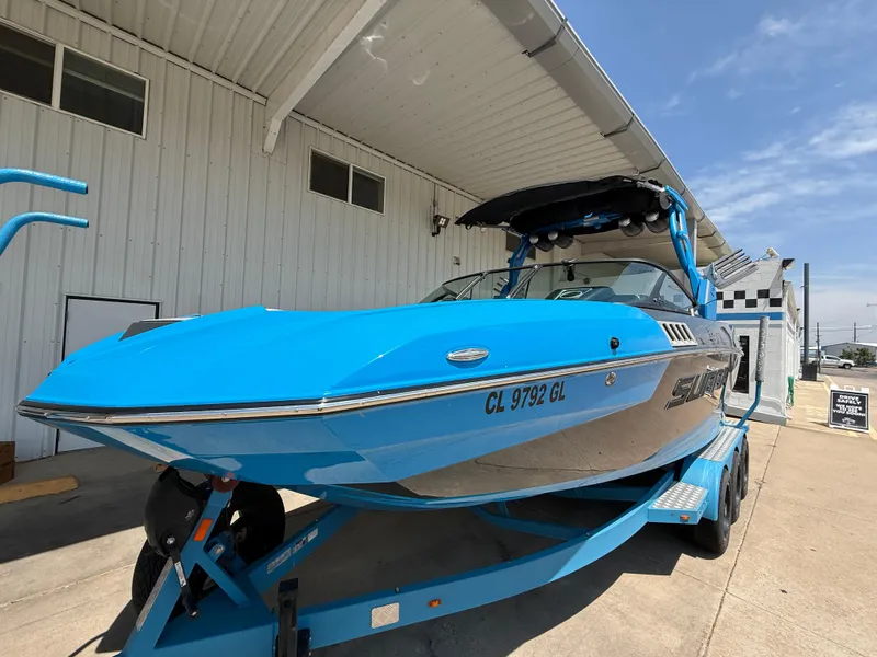 Slide: The Image of 2020 Supra SE550 boat in bright blue on trailer, parked outside a building. - 1