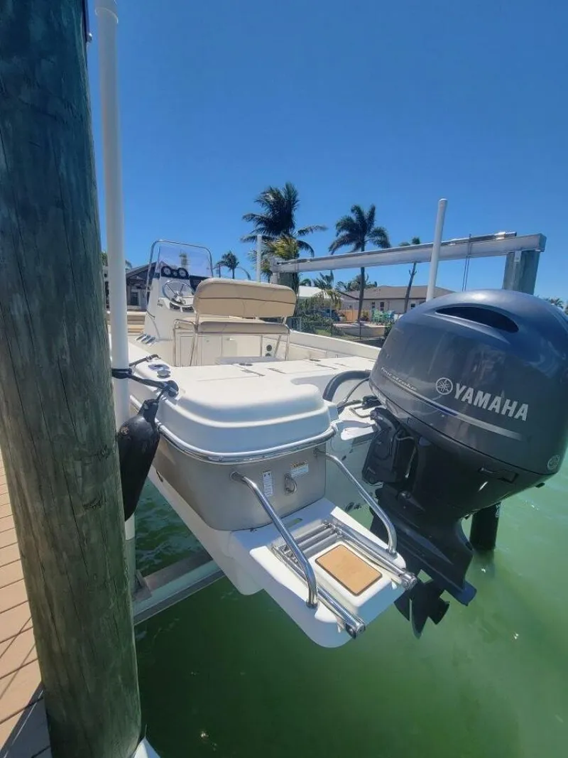 Slide: The Image of 2020 NauticStar 211 Hybrid boat with canopy on lift, docked by waterfront homes. - 3