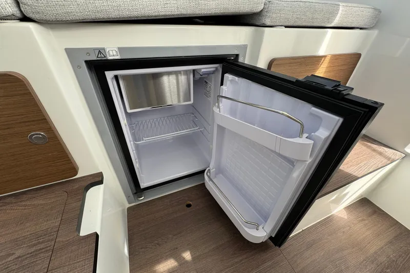 Slide: The Image of 2025 Jeanneau NC 795 SPORT S2 interior fridge, open, with wooden flooring and seating. - 10