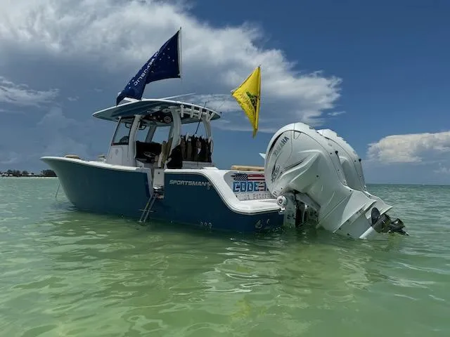 Slide: The Image of 2023 Sportsman 322 Open boat with flags, anchored in clear water under a blue sky. - 2