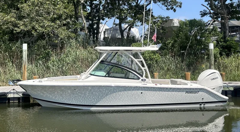 Slide: The Image of 2026 Pursuit DC 246 Dual Console boat docked by lush greenery. - 1
