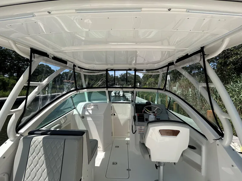 Slide: The Image of 2026 Pursuit DC 246 Dual Console boat interior with seating and helm, docked by greenery. - 18