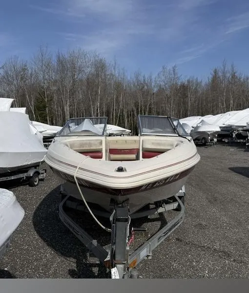 Slide: The Image of 1999 Glastron 185 boat on trailer, parked outdoors, surrounded by trees and other boats. - 3