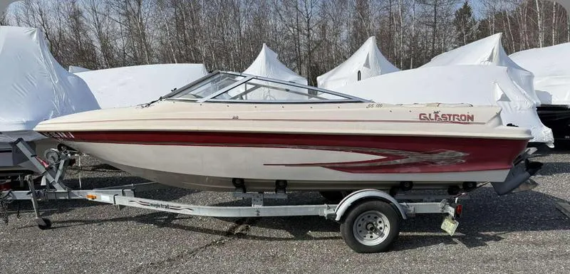 Slide: The Image of 1999 Glastron 185 boat on trailer, parked outdoors with covered boats in background. - 5