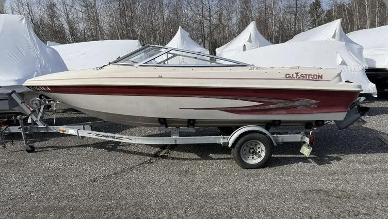 Slide: The Image of 1999 Glastron 185 boat on trailer, parked outdoors, with protective covers in the background. - 8
