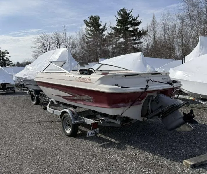 Slide: The Image of 1999 Glastron 185 boat on trailer, parked outdoors with covered boats in background. - 9