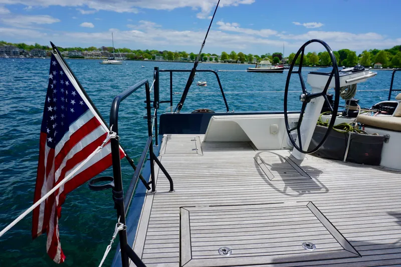 Slide: The Image of Deck of 2020 Beneteau First 53 sailboat with American flag, steering wheel, and scenic water view. - 11