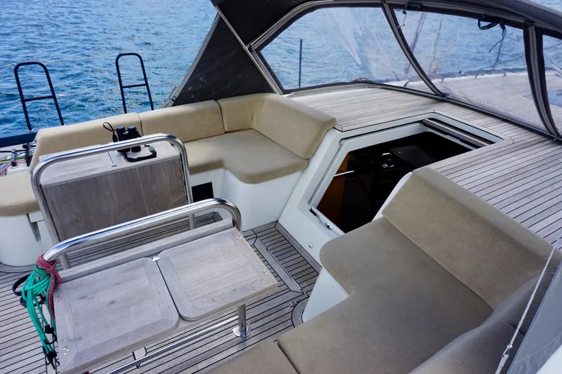 Slide: The Image of 2020 Beneteau First 53 yacht cockpit with beige seating and wooden table, overlooking the sea. - 15
