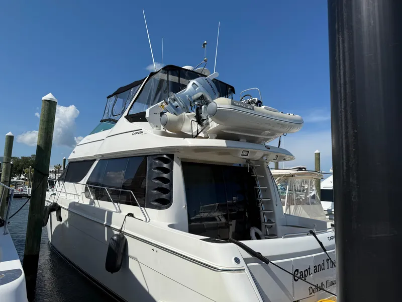 Slide: The Image of 1998 Carver 530 VOYAGER yacht docked, featuring upper deck with dinghy, clear sky background. - 6