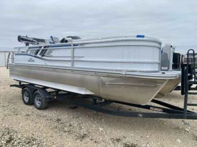 Slide: The Image of 2025 SunCatcher Select 322SS pontoon boat on a trailer, parked on gravel. - 0