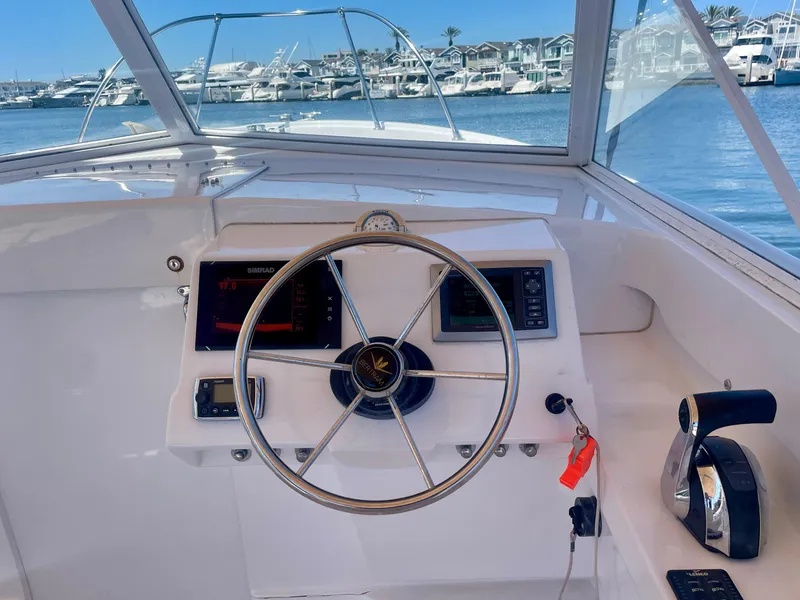 Slide: The Image of 1966 Bertram 25 Moppie boat helm with steering wheel and controls, docked in a marina. - 10