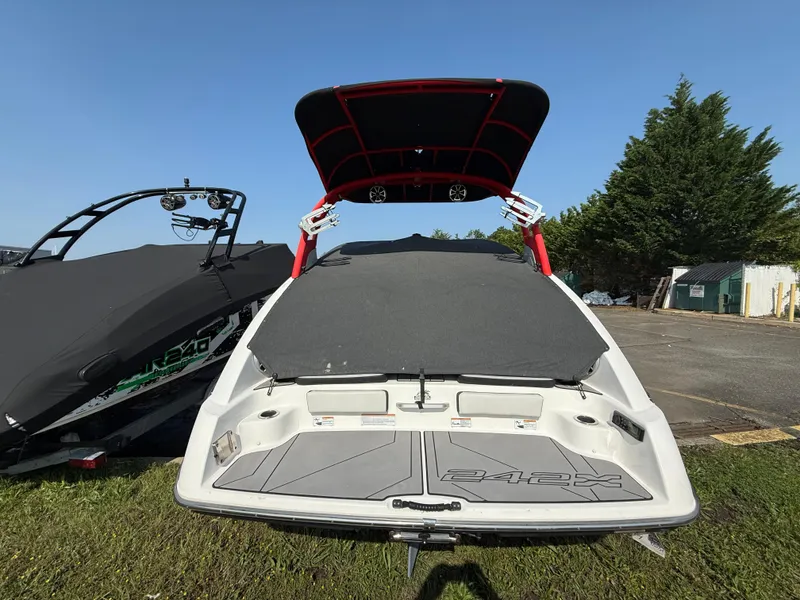 Slide: The Image of 2019 Yamaha Boats 242X E-Series, rear view, parked on grass, with covered boat beside it. - 4