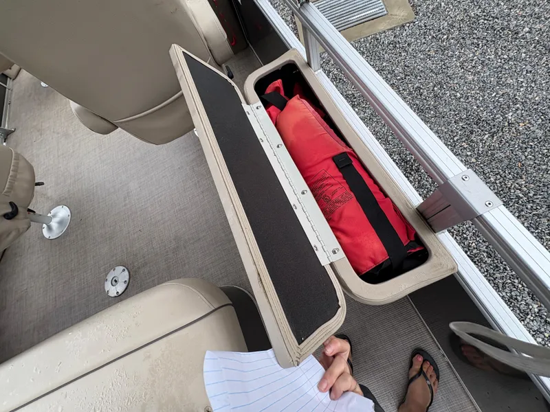Slide: The Image of Sun Tracker PARTY BARGE 2022 storage compartment with red life jacket and beige seating. - 15