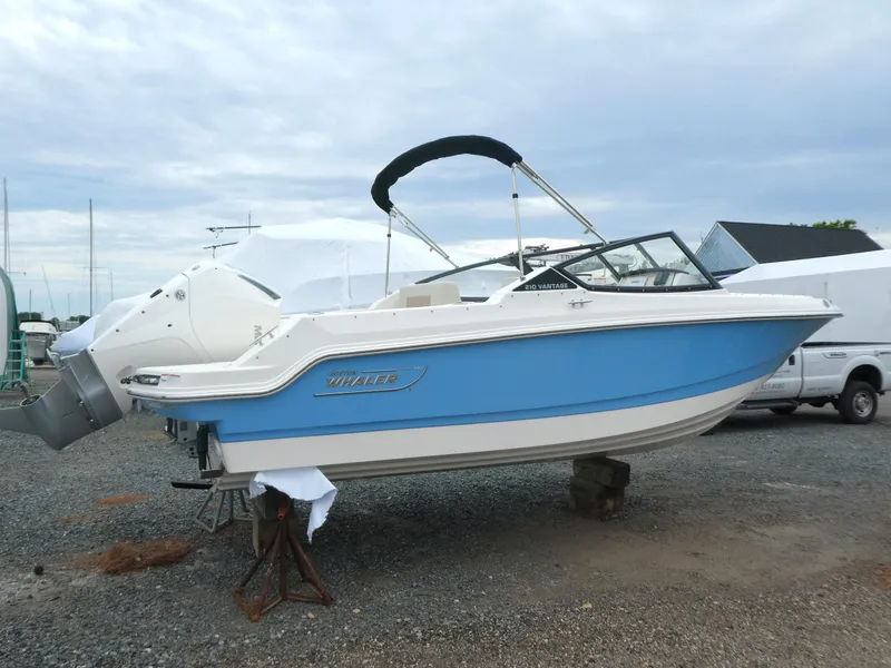 Slide: The Image of 2025 Boston Whaler 210 Vantage boat, blue and white, parked on gravel. - 1