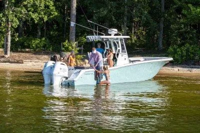 The Image of 2026 Tidewater 272 LXF boat with people enjoying a day on the water near a forested shore. - 1