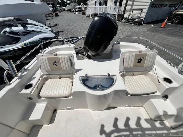 Slide: The Image of 2016 Carolina Skiff 218 DLV boat interior with seating and motor, parked outdoors. - 9