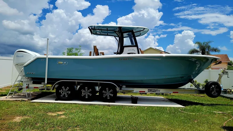 The Image of 2022 Sea Hunt Gamefish 30 boat on trailer, blue hull, parked on grass under cloudy sky. - 0