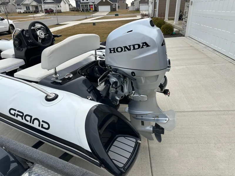 Slide: The Image of 2022 Grand Inflatables G380 with Honda outboard motor, parked on a driveway. - 2