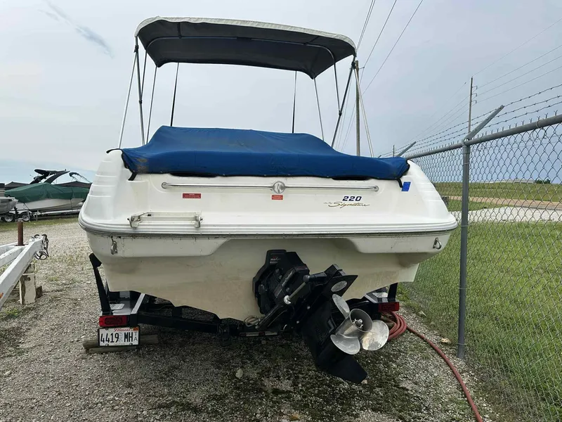 Slide: The Image of 1994 Sea Ray 220 Bow Rider boat with blue cover, parked on gravel near a fence. - 28