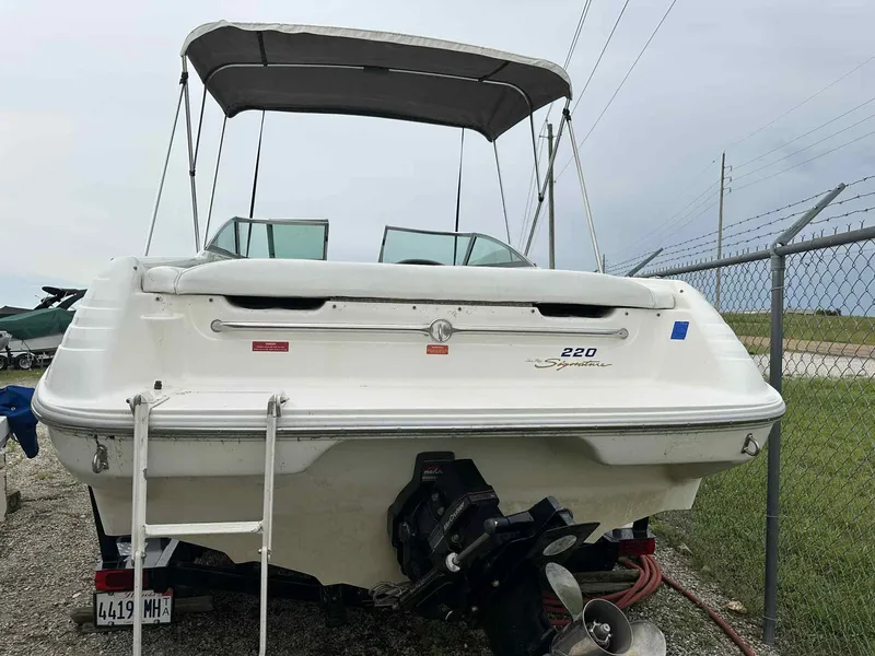 Slide: The Image of 1994 Sea Ray 220 Bow Rider boat with canopy, parked on gravel near a fence. - 6