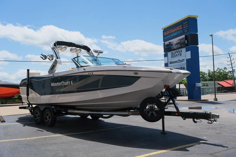 Slide: The Image of 2025 MasterCraft X26 boat on trailer at dealership under clear blue sky. - 13