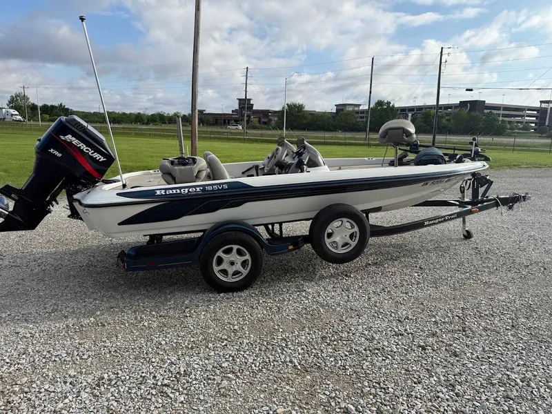 Slide: The Image of 2003 Ranger 185 VS boat on trailer with Mercury outboard motor, parked on gravel. - 1