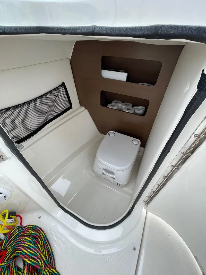 Slide: The Image of 2013 Sea Ray 240 Sundeck interior with compact toilet and storage shelves. - 20
