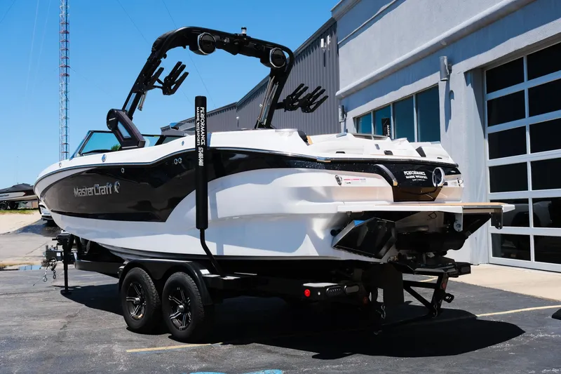 Slide: The Image of 2023 MasterCraft X24 boat on trailer, parked outside a building under clear blue sky. - 5