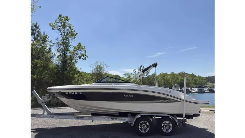 Slide: The Image of 2016 Sea Ray SPX 210 boat on trailer, parked near a lake with trees in the background. - 0