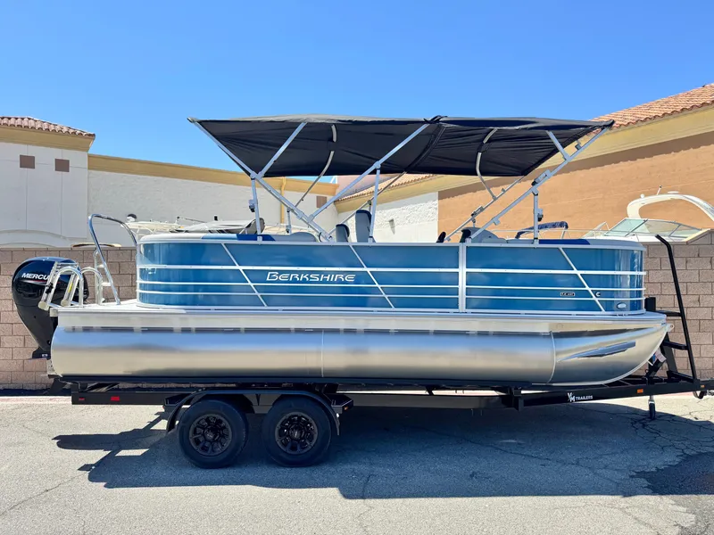 Slide: The Image of 2025 Berkshire 22RFX LE pontoon boat on trailer, featuring a sleek blue design and canopy. - 0