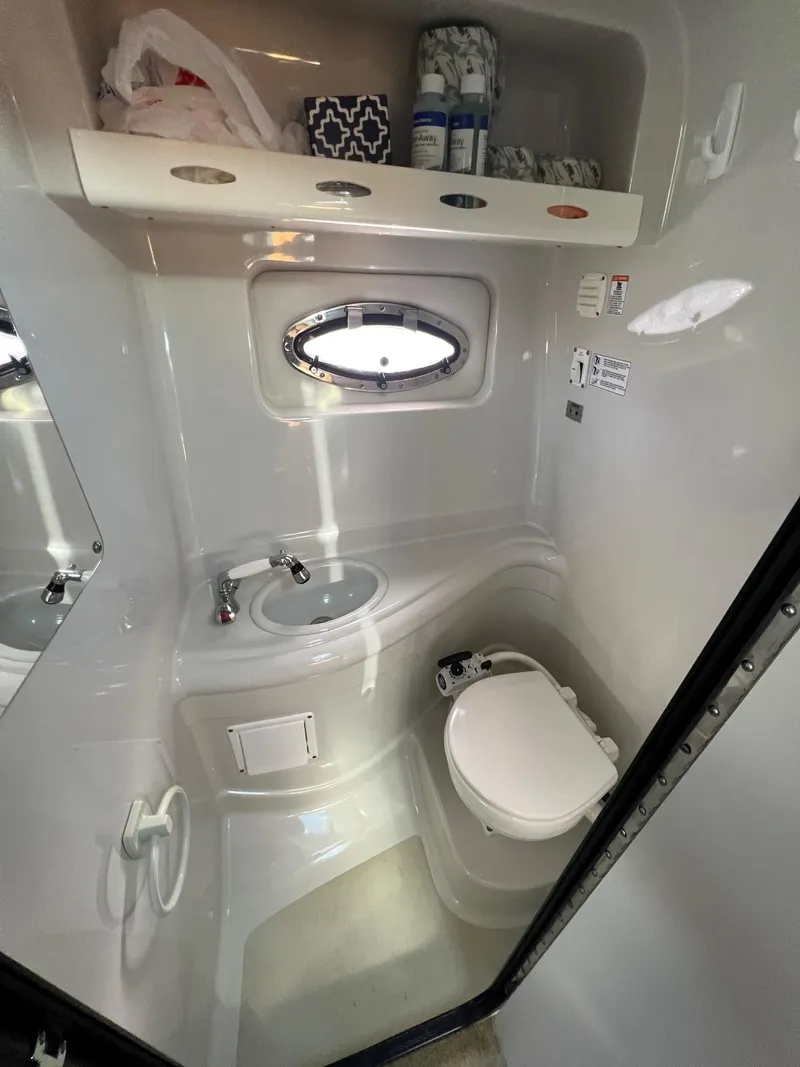 Slide: The Image of Compact bathroom in a 2008 Crownline 270 CR boat with sink, toilet, and porthole window. - 23