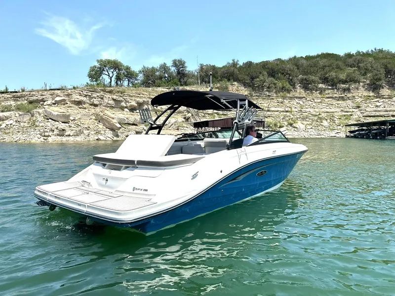 Slide: The Image of 2020 Sea Ray SPX 230 boat cruising on a sunny lake with rocky shoreline. - 11