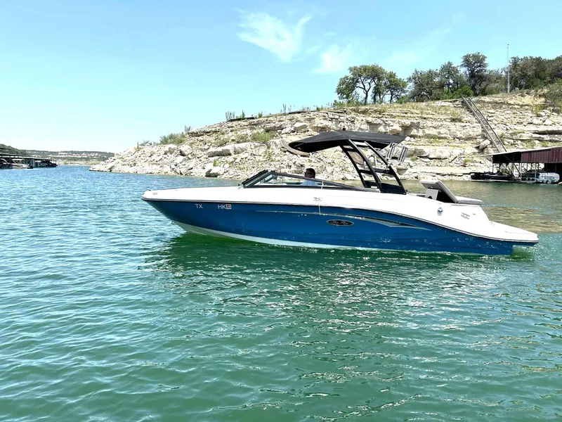 Slide: The Image of 2020 Sea Ray SPX 230 boat cruising on a sunny lake with rocky shoreline. - 16