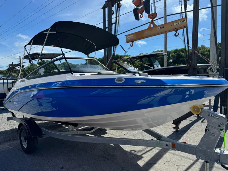 Slide: The Image of 2025 Yamaha Boats SX195, blue and white, on trailer under sunny sky. - 1