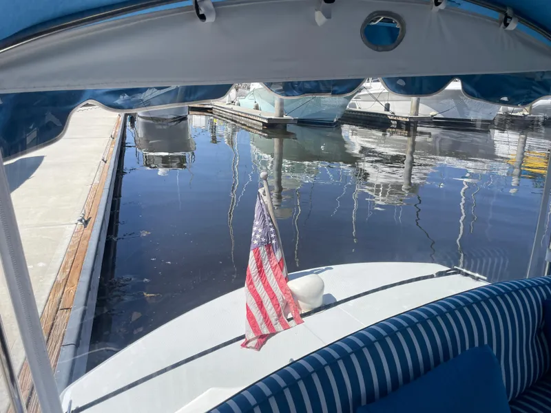 Slide: The Image of 2014 Duffy 18 Snug Harbor boat docked, featuring striped seating and American flag. - 16