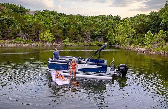 Slide: The Image of 2025 Lowe LS 190 pontoon boat on trailer, parked outside a building. - 2
