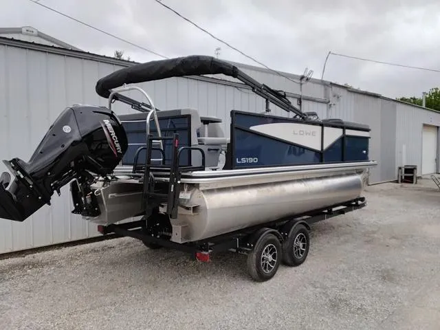 Slide: The Image of 2025 Lowe LS 190 pontoon boat on trailer, parked outside a warehouse. - 3
